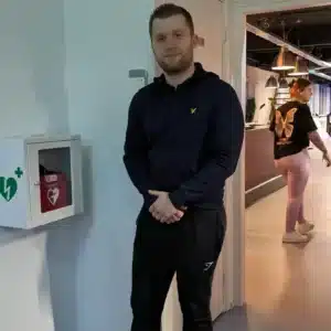 Man poseert voor een wandkast met Philips AED in een fitnessruimte.