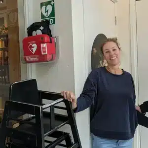 Vrouw staat binnen naast een wandgemonteerde Philips AED in houder met AED-bord erboven.