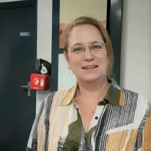 Vrouw glimlacht voor een muur met een gemonteerde rode Philips HeartStart AED in wandkast.