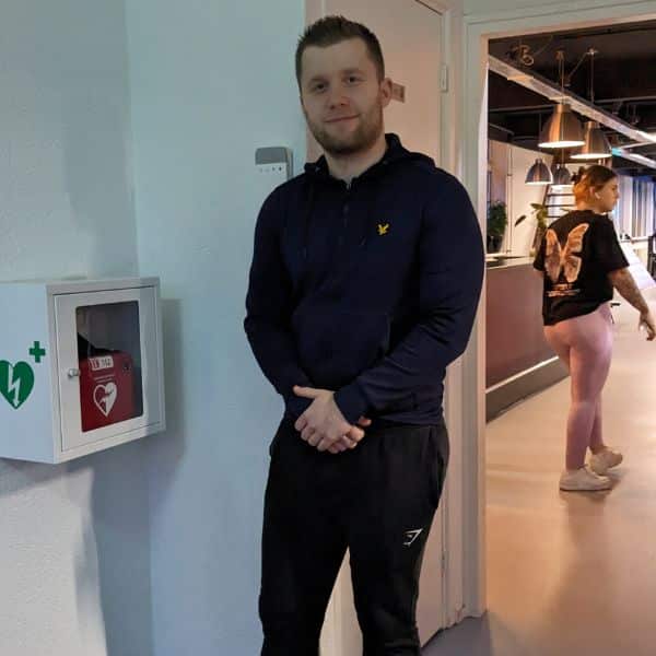 Man poseert voor een wandkast met Philips AED in een fitnessruimte.